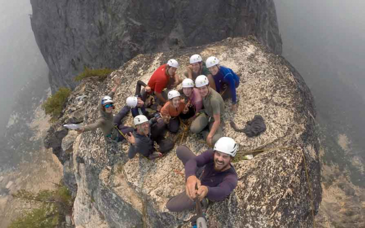 a group of climbers smile as they celebrate reaching the summit 
